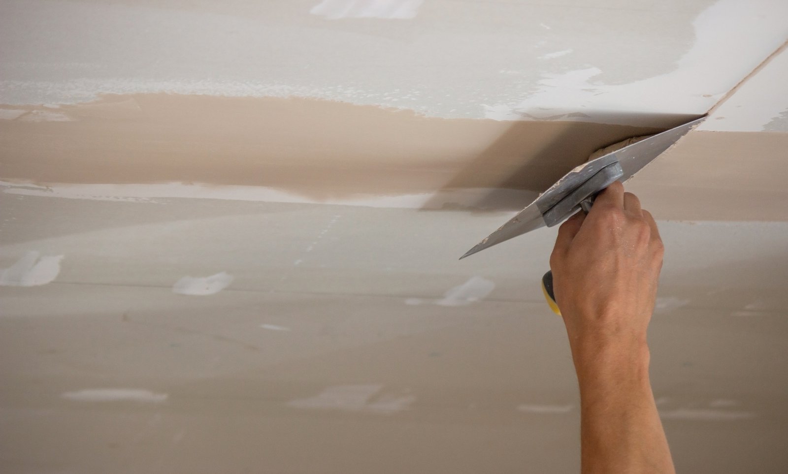 Un homme met du mastic sur un plafond en plaques de plâtre. Mastic pour les joints des plaques de plâtre